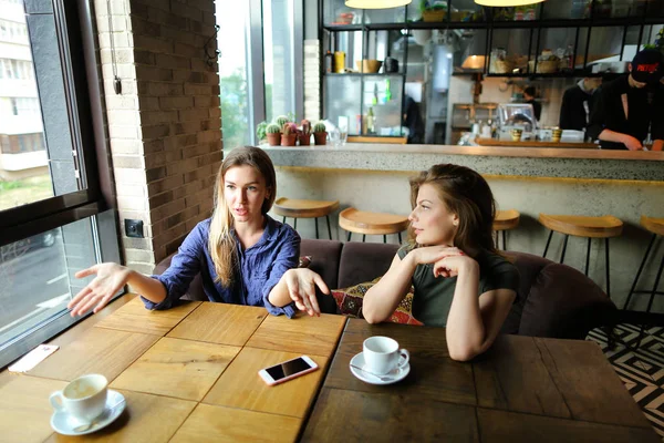 Позитивні приємні жінки сидять в кафе з чашками кави і посміхаються . — стокове фото