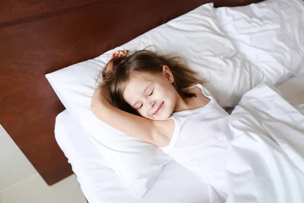 Маленькая девочка спит утром перед школой на кровати с белым бельем . — стоковое фото