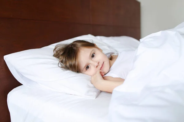 Gadis Kaukasia kecil tidur di pagi hari sebelum sekolah di tempat tidur dengan linen putih . — Stok Foto