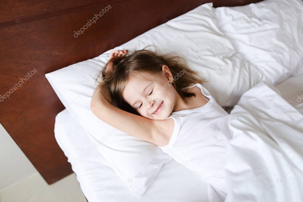 Little girl sleeping in morning before school on bed with white linens.