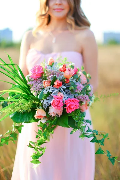 Wanita cantik berdiri dengan karangan bunga mengenakan gaun merah muda . — Stok Foto