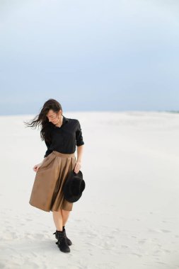 Kar üzerinde duran ve beyaz arka planda kahverengi etek, siyah bluz ve tutma şapka giyen sevimli güzel kız.