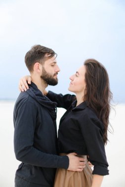 Birbirlerine sarılma ve etek giyen ve şapka tutmak bir kadın beyaz kış arka planda duran genç mutlu çift.