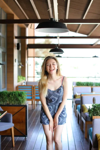 Mujer sonriente de pie en la cafetería cerca de sillones y plantas de la habitación . — Foto de Stock