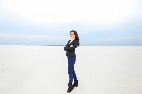 Joven mujer de negocios agradable de pie sobre la nieve en el fondo monótono, con gafas . —  Fotos de Stock