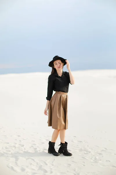 Caucasiano menina bonita usando saia, blusa preta com chapéu e de pé na neve . — Fotografia de Stock