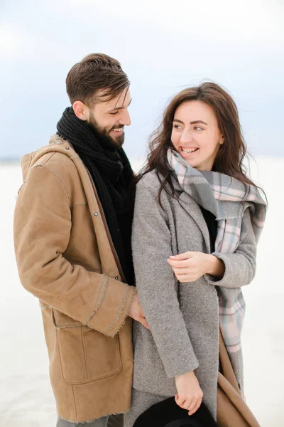 Glücklicher Kerl umarmt weibliche Person trägt grauen Mantel und Schal, weißen Winter monophonen Hintergrund. — Stockfoto