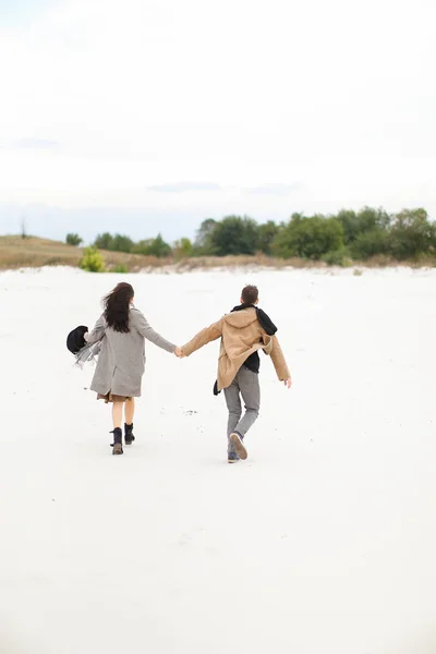 Feliz pareja joven caminando en invierno fondo blanco, tomados de la mano y usando abrigos . — Foto de Stock