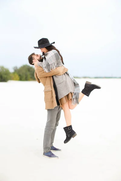 欧洲男子拾起年轻女子戴着帽子, 大衣和灰色围巾在白雪背景. — 图库照片