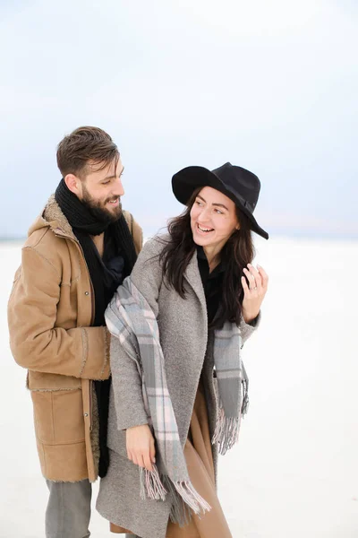 Leende ung kvinna och man med skägg bär kappor och scarfs stående i vinter snö bakgrunden. — Stockfoto