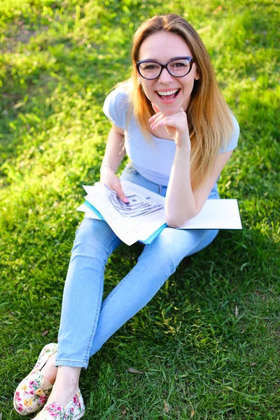 Female landscape designer sitting on green grass with documents in park and keeping money.