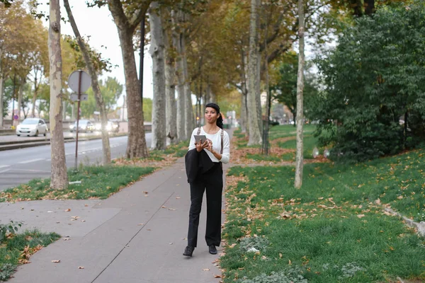 Afroamerikanerin schöne Studentin geht mit Tablet im Herbst Park, trägt Rucksack. — Stockfoto