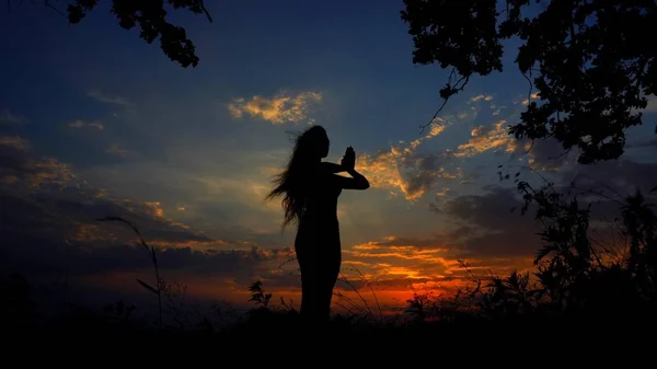Тёмный женский силуэт, занимающийся йогой и медитирующий на фоне вечернего неба . — стоковое фото