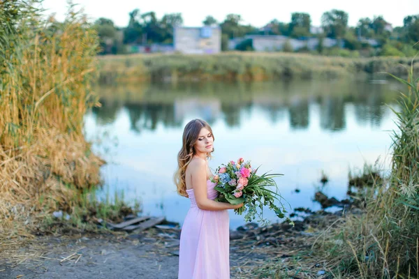 Έγκυος γυναίκα που φοράει ροζ φόρεμα με μπουκέτο από λουλούδια που στέκεται κοντά στη λίμνη. — Φωτογραφία Αρχείου