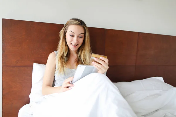 Концепція молодої жінки збирається купувати онлайн з планшетом і дебетовою карткою, сидячи в ліжку . — стокове фото