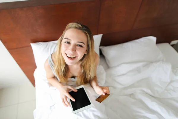 신용 카드, 침대에 앉아 태블릿 온라인 및 지불 것을 구입 하는 젊은 행복 한 여자. — 스톡 사진