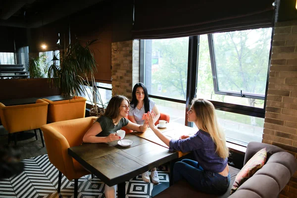 Junge Freundinnen sprechen im Café und benutzen Smartphone, trinken Kaffee. — Stockfoto