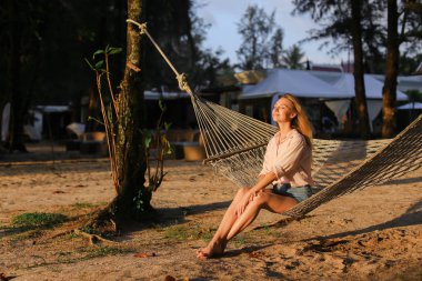 Genç Amerikalı yalınayak kadın beyaz hasır hamakta kum üzerinde dinlenme.