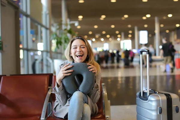 Woman sitting with neck pillow and luggage in airport waiting room. — Stock Photo, Image