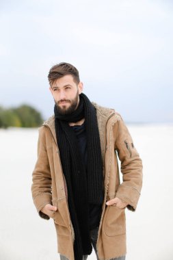Paltonu ve kaşkolünü beyaz kar arka planda duran giyen sakallı Avrupa erkek kişi.