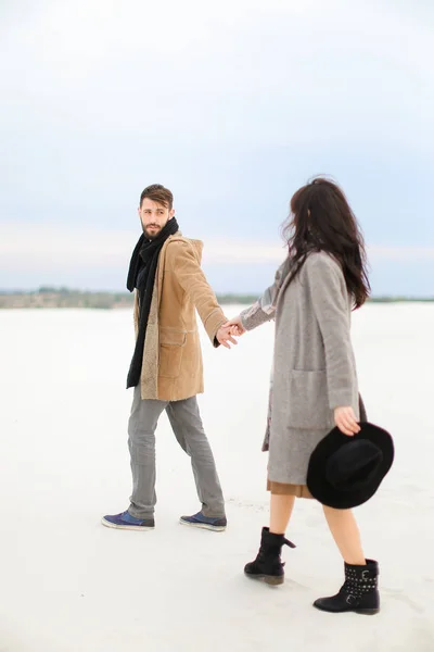 若い男と女が起こって雪と手を取り合って、着ているコートし、スカーフ. — ストック写真