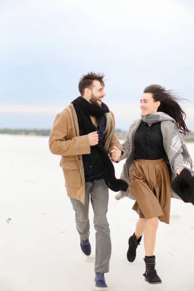 Щасливий молодий чоловік і жінка бігають на снігу і носять модний одяг, зимовий фон . — стокове фото