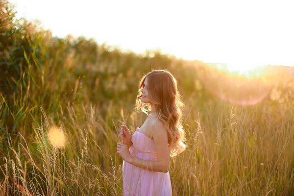 Pregnant female person standing in sun rays with steppe background, wearing pink dress. Concept of gentle summer photo session and pregnance.