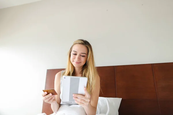 Fiatal blonde boldog nő vásárol dolog online tabletta és a kifizető a hitelkártya. — Stock Fotó