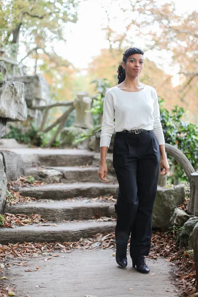 Beautiful black girl wearing white blouse standing near stone stairs in park.