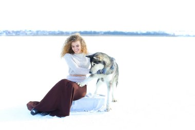 Beyaz kar arka planda husky ile oturan kadın.