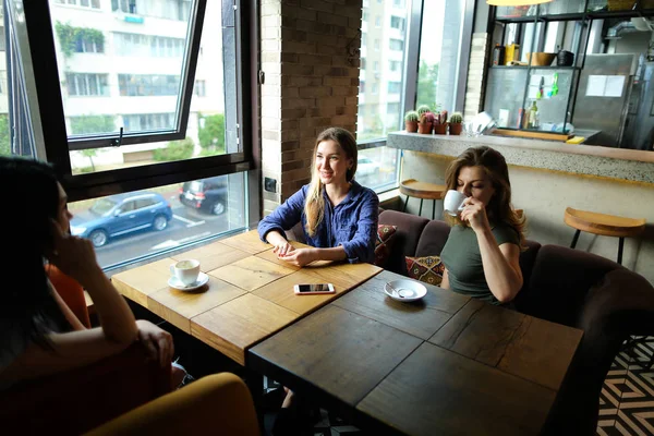 Encantadoras mujeres sentadas en el restaurante y hablando con tazas de café . — Foto de Stock