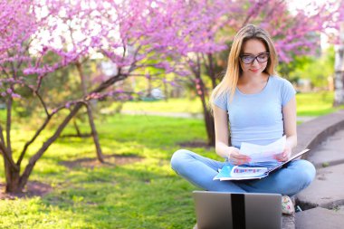 Dizüstü bilgisayar ve çiçek açan park gazetelerde okuyan kız öğrenci.