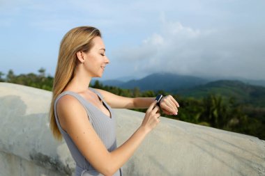 Genç kadın akıllı seyretmek, arka planda yeşil mouintains arıyor.
