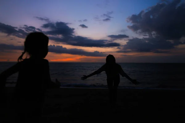 Silhouette of young female person and girl on sea shore in sunset. — Stock Photo, Image