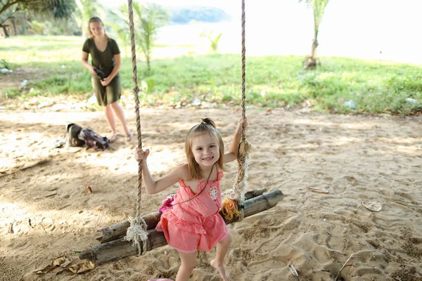 Mała dziewczynka jazda na huśtawce na piaszczyste podłoże, sukience różowy. — Zdjęcie stockowe
