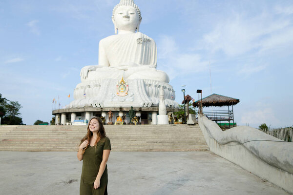 Young woman in khaki dress standing near concrete statue of Buddha in Phuket.