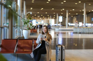 Havaalanı hall yanında valiz tablet ile internet kullanan genç kız.