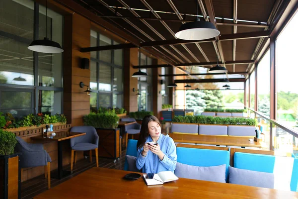 Estudiante inteligente bebiendo café en la cafetería y sentada con teléfono inteligente y portátil . — Foto de Stock