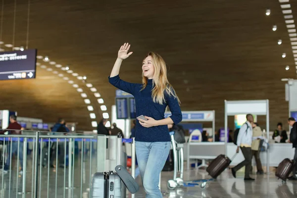 Stojący w hali lotniska z smartphone, walizka i podniósł rękę studenta. — Zdjęcie stockowe