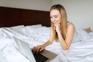 Dizüstü bilgisayar kullanarak ve sabah yatakta yatarken genç kadın.