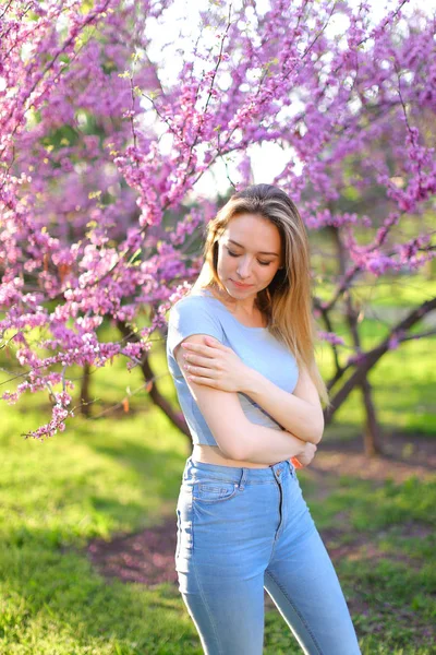 Мечтающая блондинка фотомодель, стоящая в парке с цветущим фоном . — стоковое фото