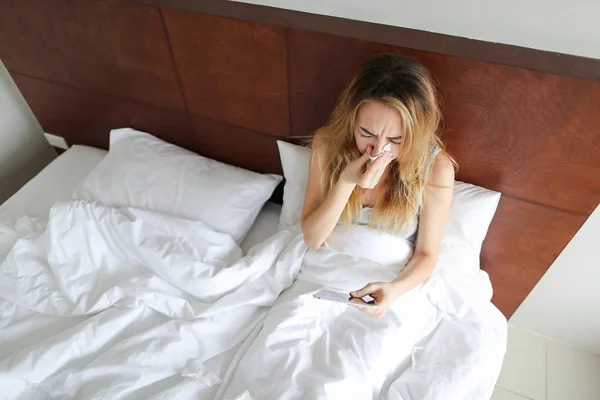 Молодая женщина сидит в постели, чихает с салфетками . — стоковое фото