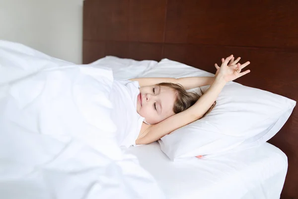 Menina encantadora com as mãos levantadas dormindo na cama com lençóis brancos de manhã . — Fotografia de Stock