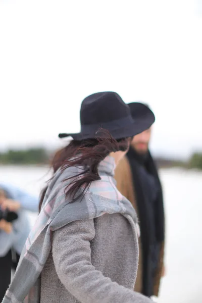 Joven mujer feliz con sombrero y abrigo gris con bufanda de pie en el fondo blanco de invierno . — Foto de Stock