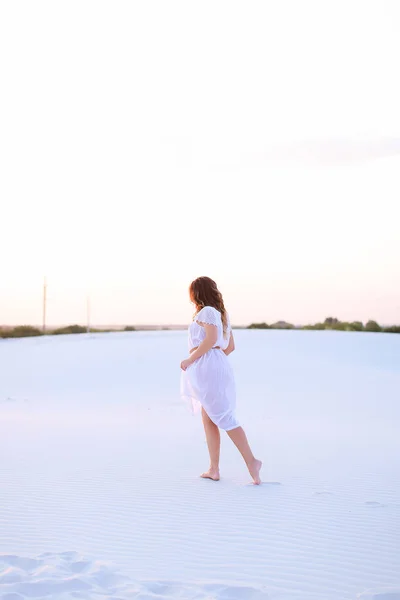 Young female person wearing white dress walking barefoot on sand