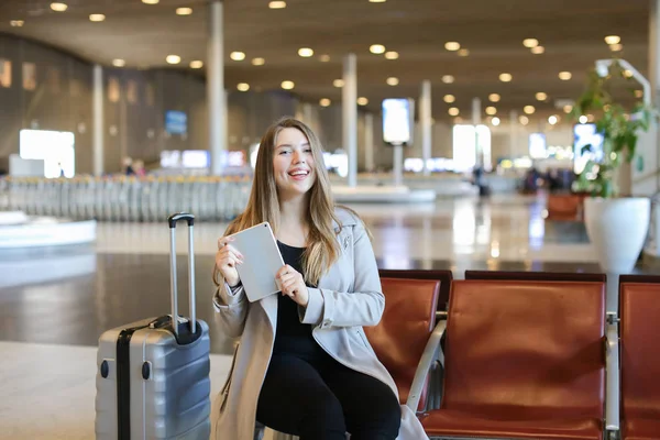 Uśmiechnięta kobieta, korzystanie z Internetu przez tablet w hali lotniska w pobliżu walizka. — Zdjęcie stockowe