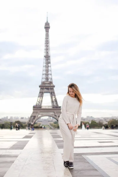 Stylish caucasian girl standing near Eiffel Tower in white overalls. — Stock Photo, Image