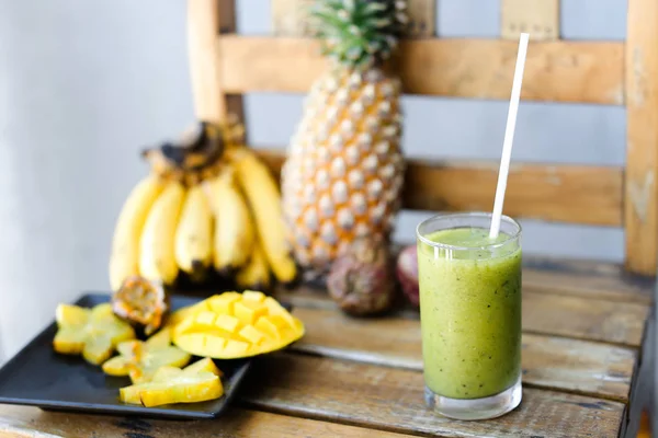 Tasty bananas, carambola with pine apple and mango on wooden chair, green fresh kiwi juice.