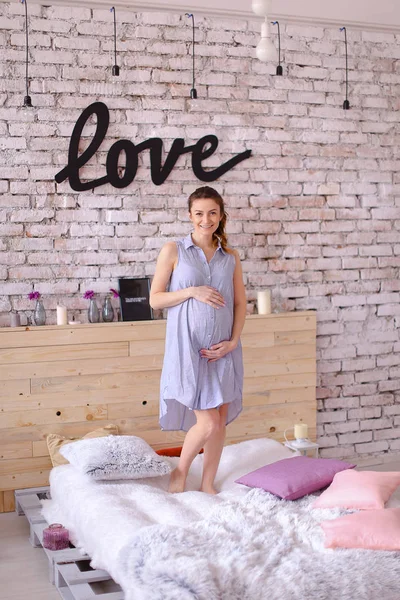 Grávida encantadora mulher vestindo vestido azul segurando barriga, amor inscrição na parede de tijolo . — Fotografia de Stock