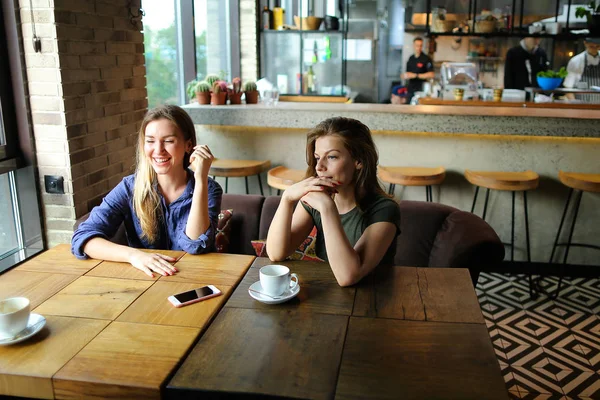 Positive hübsche Frauen sitzen mit Tassen Kaffee im Café und lächeln. — Stockfoto